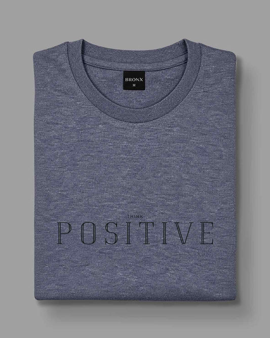 Polera Think Positive gris azulado de BRONX, doblada, con estampado frontal visible.